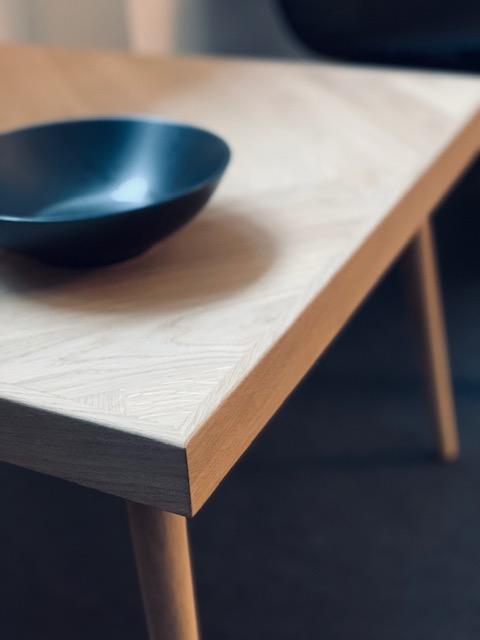 Et moderne træbord med en sort skål placeret på toppen, set fra en skrå vinkel.