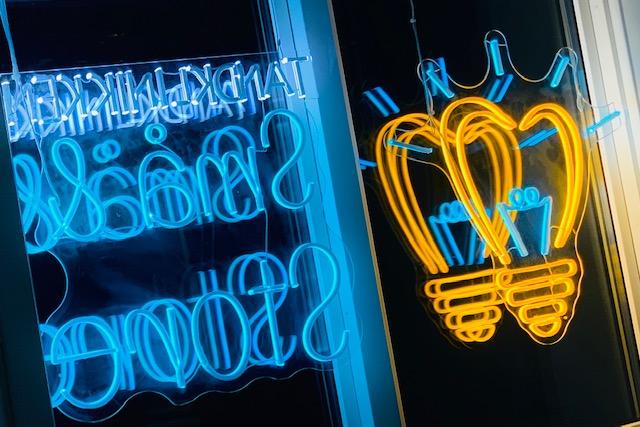 Neonlys med teksten "Salg" i blå og hjerteformede pærer i orange, der hænger i vinduet.
