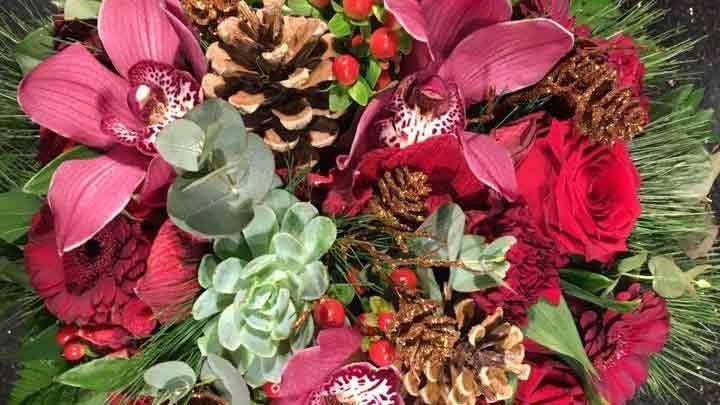 En smuk buket med røde roser, orkideer, fyrrekogler og grønne planter, perfekt til dekoration.