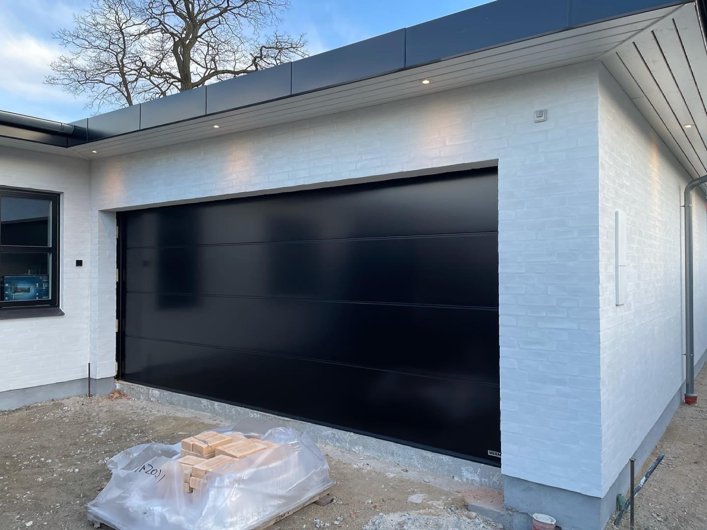 Nybygget garage med sort garageport og hvid murstensvæg, beliggende på en byggeplads.