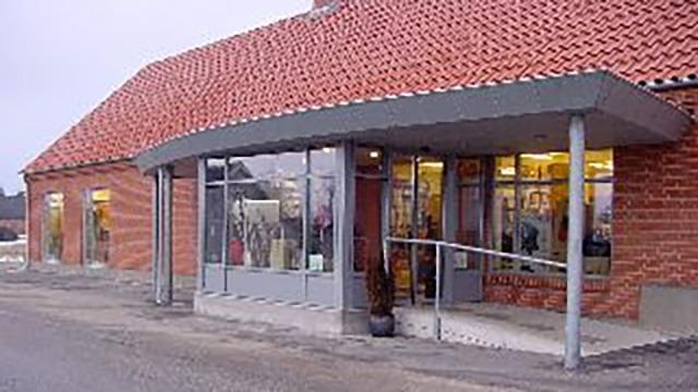 En butik med glasfacade og skråning ved indgangen, beliggende i et rødt murstenshus med tag af tegl.