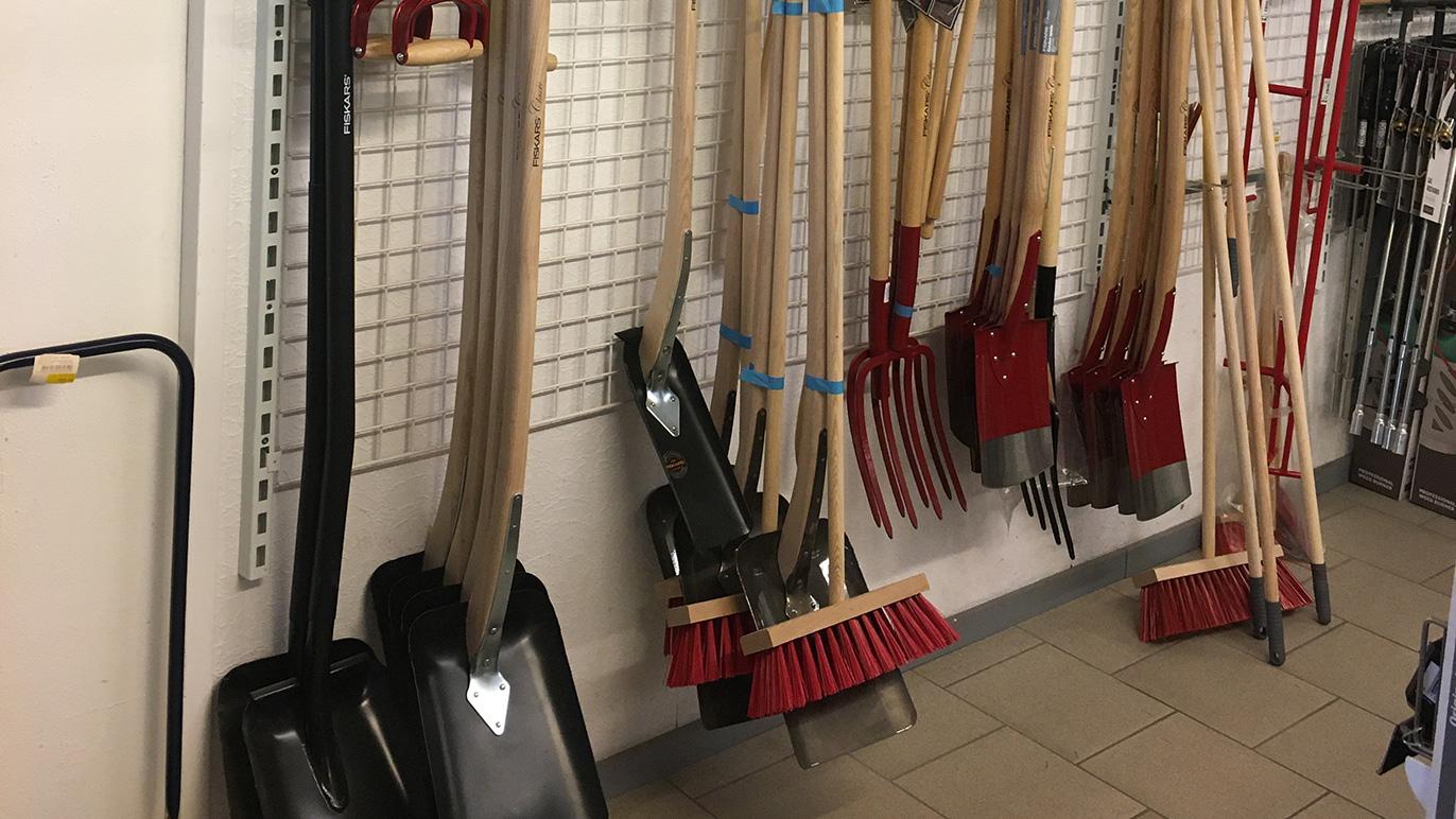 Værktøjsvæg med forskellige redskaber som koste, skovle og greb i en butik.