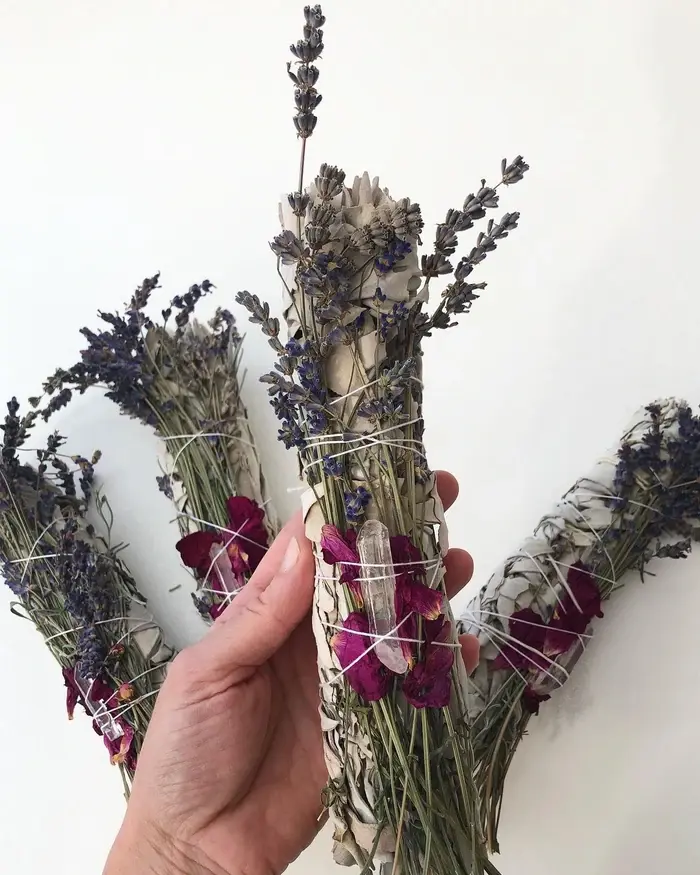 Hånd, der holder en bundt af lavendel og tørrede blomster, bundet med snor på en hvid baggrund.