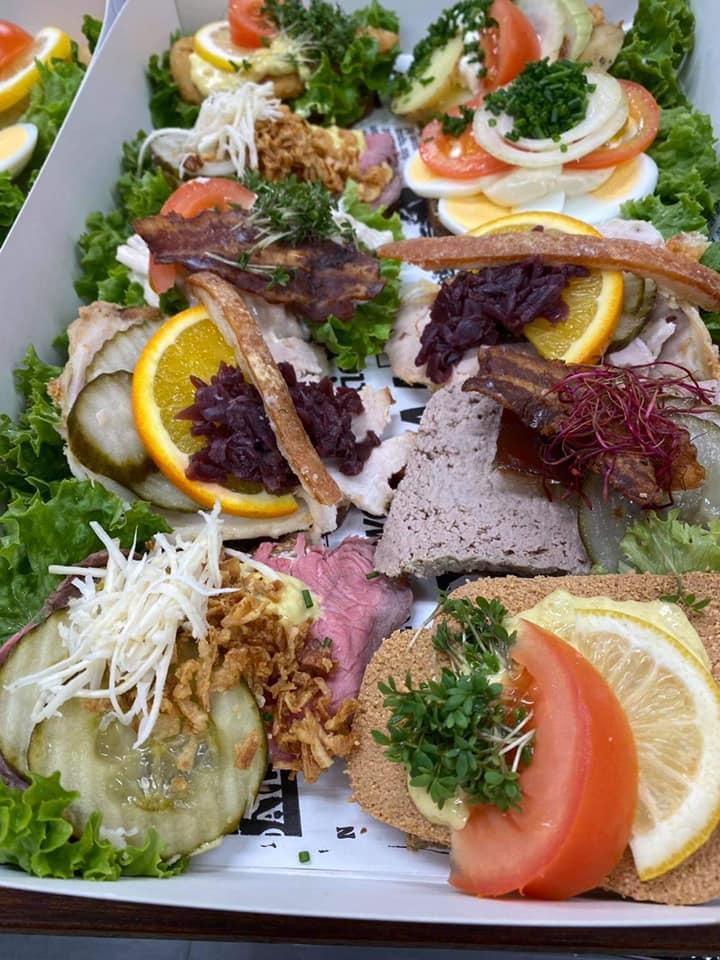 En farverig anretning med forskellige smørrebrød, salat, grøntsager og pynt som citron og persille.
