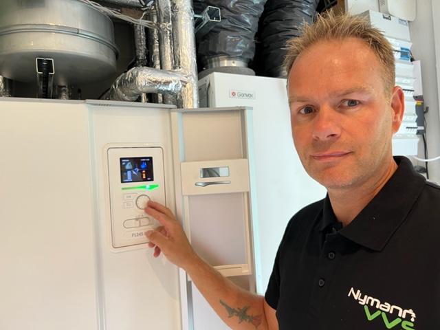 En mand justerer indstillingerne på en moderne varmepumpe i et teknisk rum.