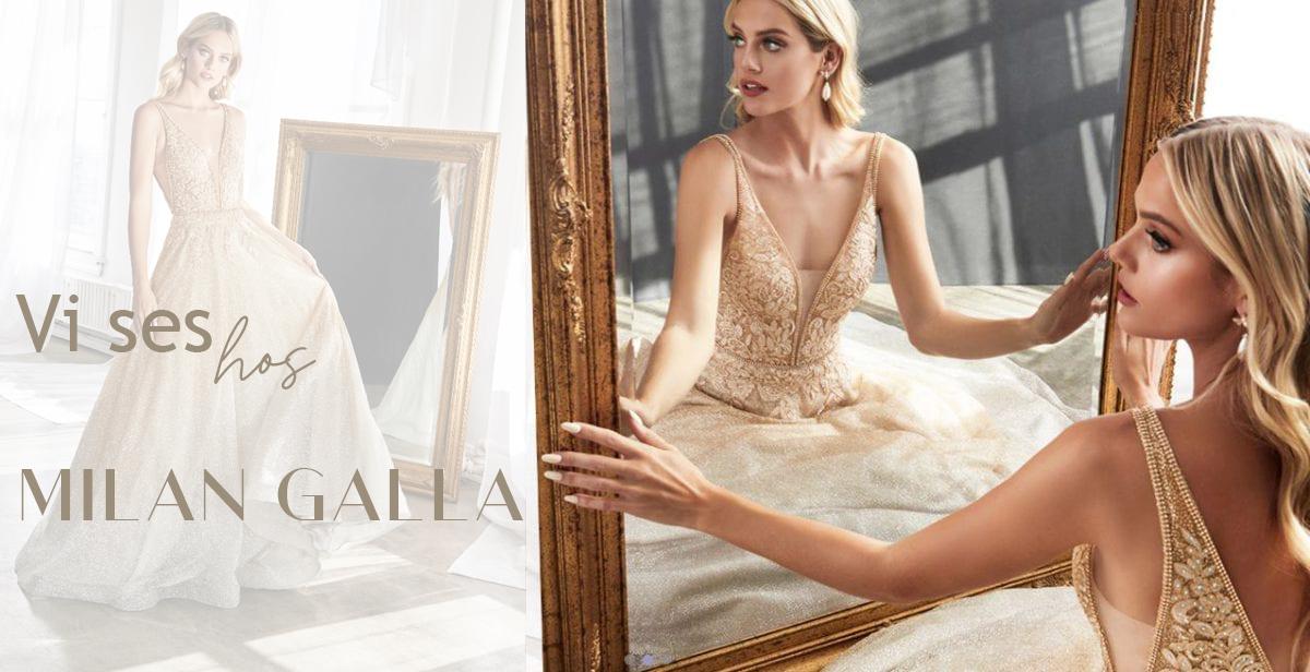 En smuk brudekjole præsenteres af en model foran et spejl i en elegant setting.