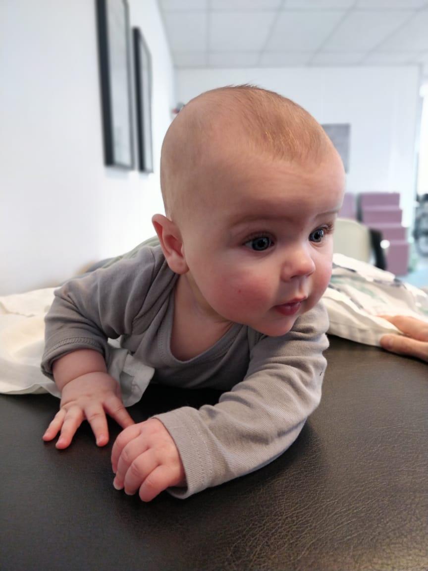 En baby i grå tøj, der kravler på en sort overflade med nysgerrige øjne og en sød ansigtsudtryk.