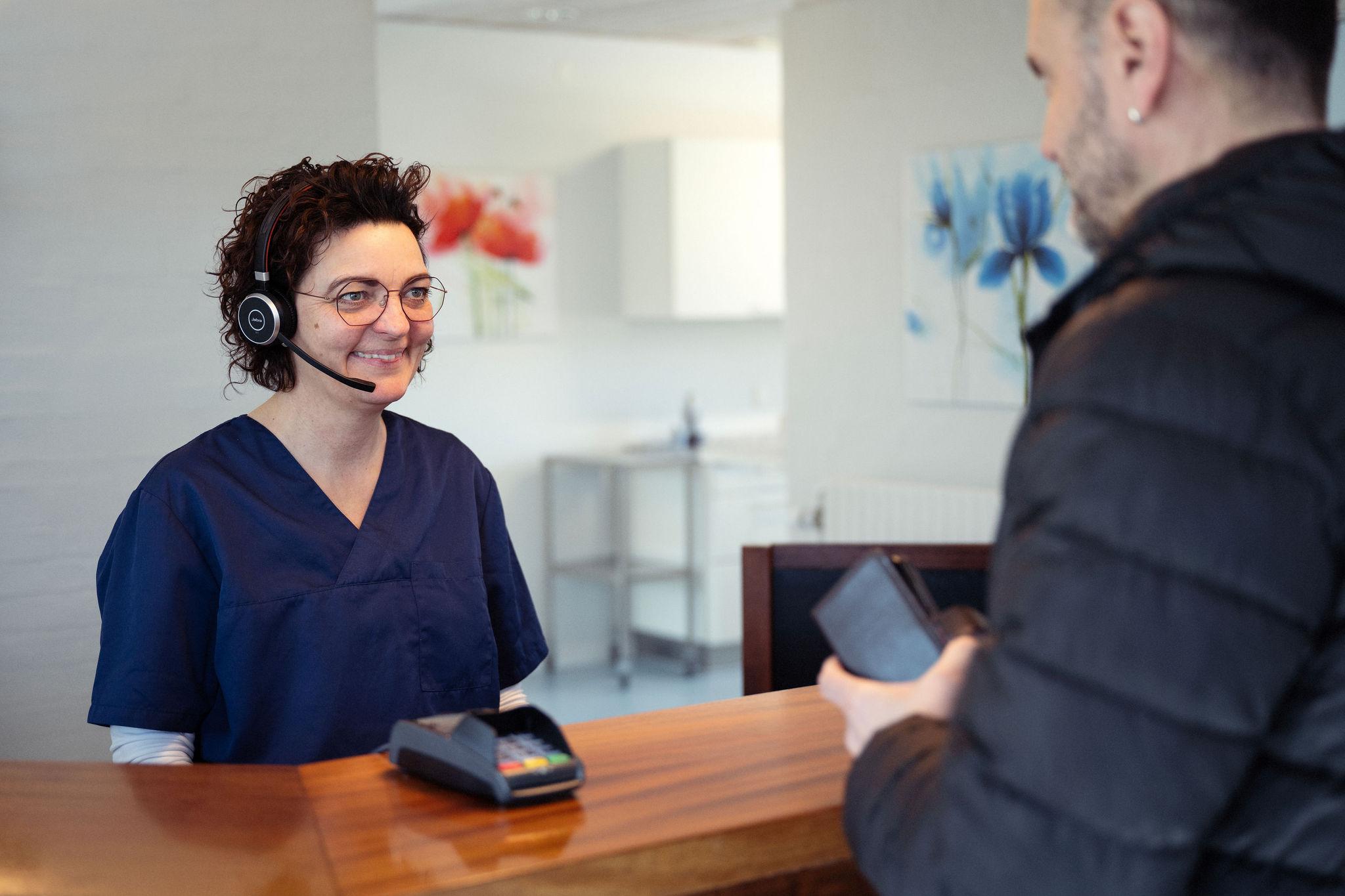En receptionist med headset smiler til en kunde ved skranken i en moderne klinik.