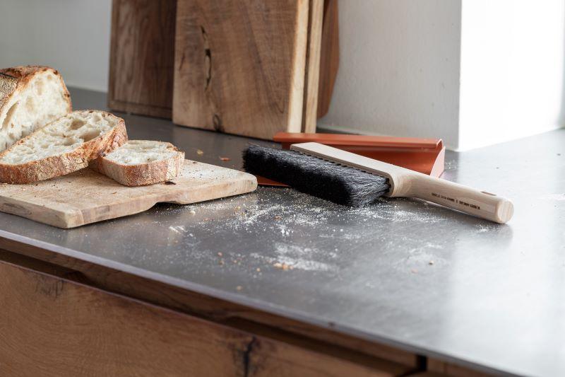 Et køkkenbord med skiver af brød, en brødbørste og melrester på overfladen.