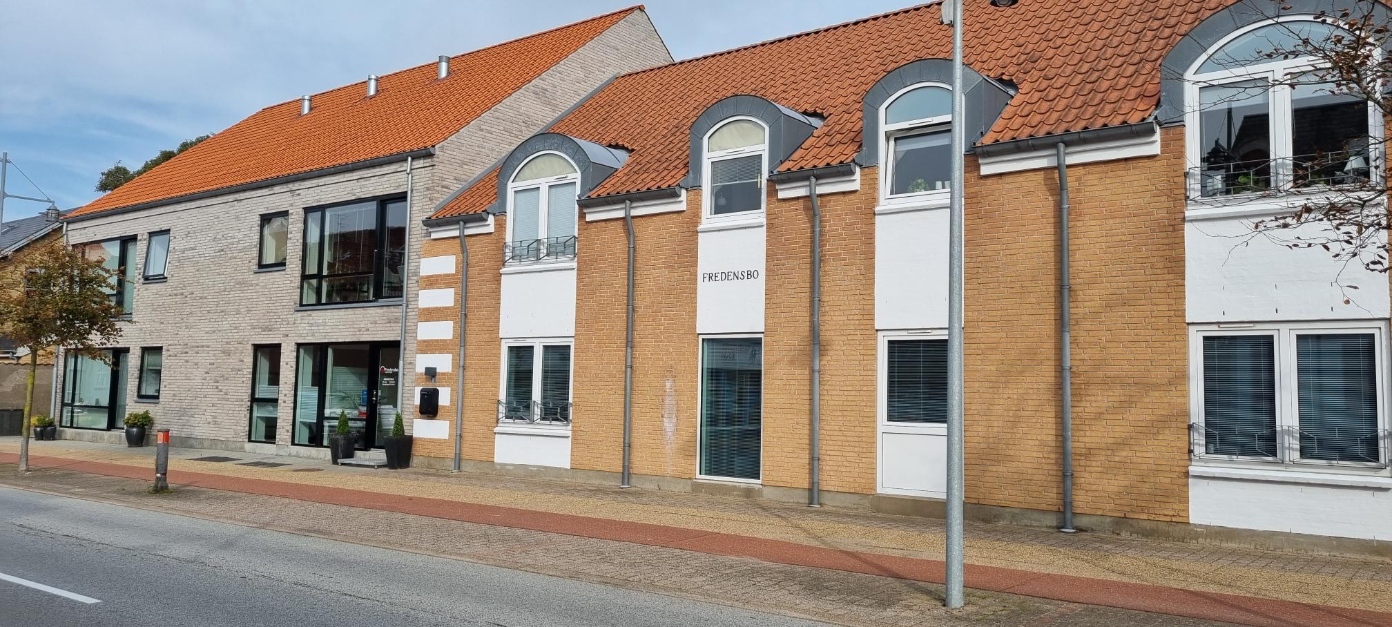 Moderne bygninger med røde tage og store vinduer langs en gade.