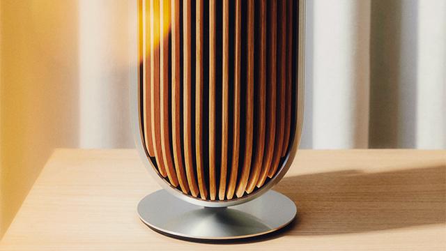 Moderne bordlampe med trælameller og metalbund, der kaster et varmt lys i et stilrent rum.
