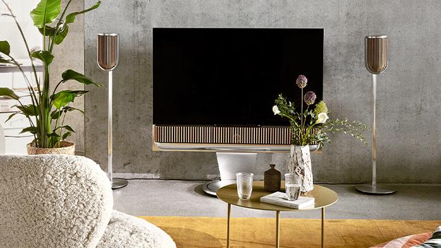 Moderne stue med en stor tv-skærm, dekorative planter og en elegant kaffebord med blomster og glas.