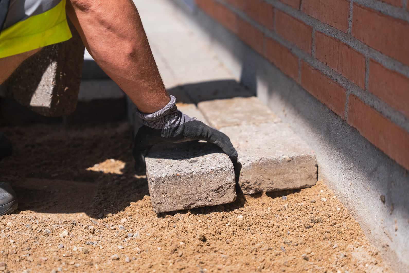 En hånd lægger betonsten på sand under opbygning af en mur.