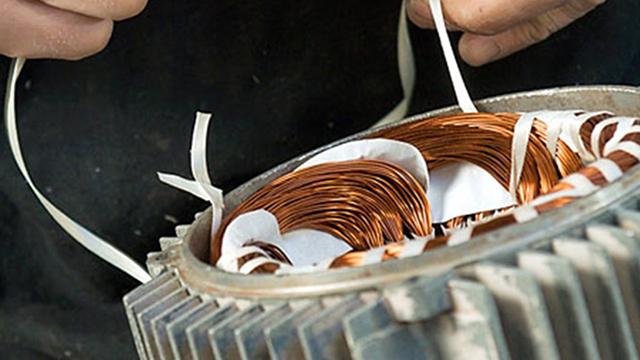 Hænder der arbejder med kobberledninger i en elektrisk motor, der viser detaljer af viklinger og isolering.