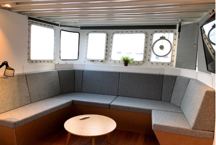 Moderne stue med grå sofa, rundt bord og store vinduer, der giver naturligt lys.