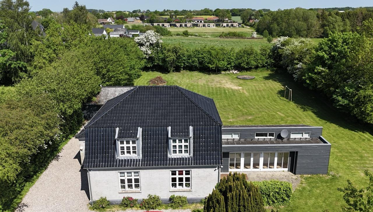 Moderne hus med sort tag og stor have, omgivet af grønne træer og græsarealer.