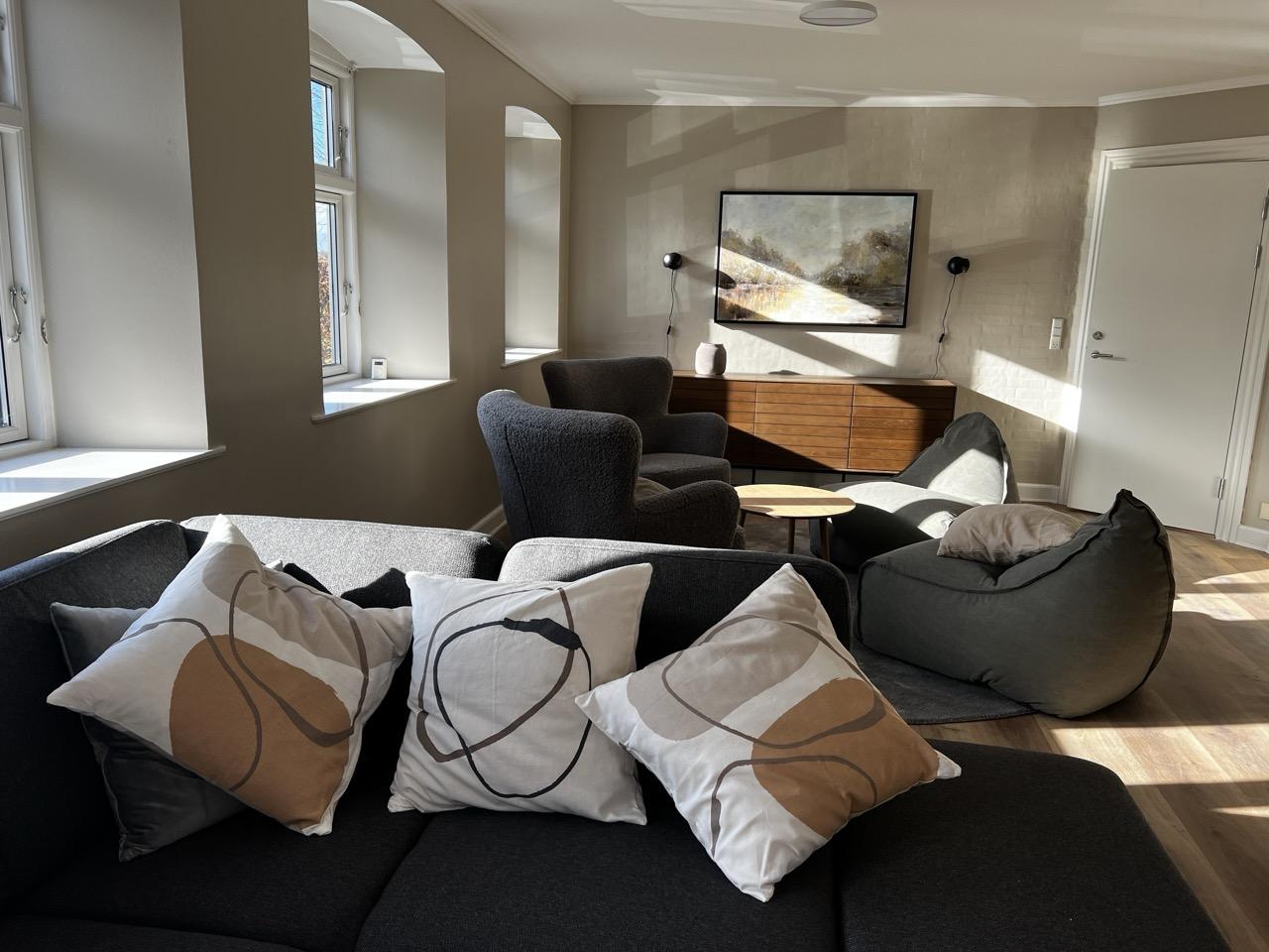 Lys stue med moderne møbler, herunder en sofa med puder, lænestole og et rundt bord.