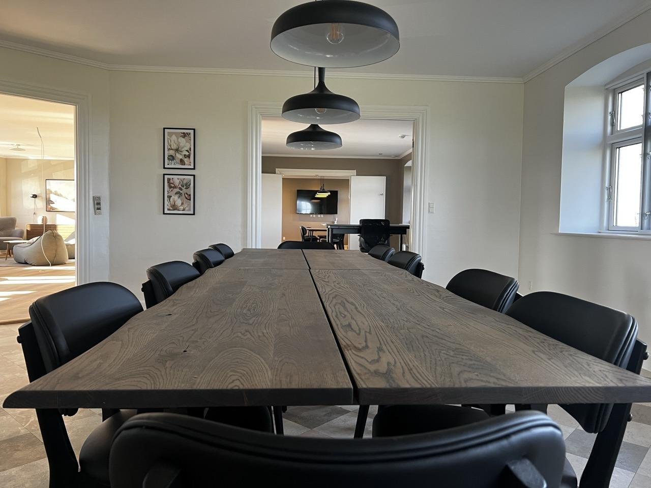 Et moderne spisestue med et langt træbord og sorte stole, belyst af stilfulde lamper.