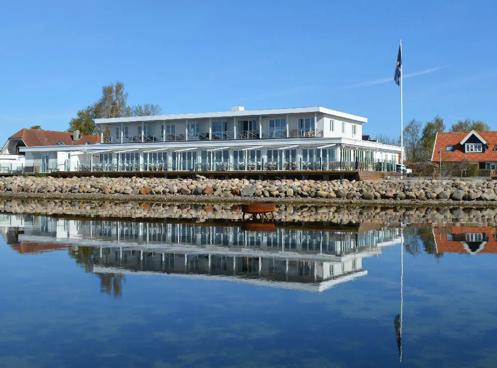 Moderne bygning ved vandet med spejlbillede i roligt vand og klar blå himmel.