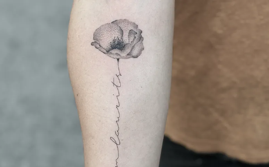 En tatovering af en blomst med detaljeret skygge og teksten "moments" skrevet under.