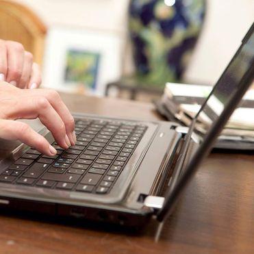 Hænder der skriver på et bærbart computer tastatur på et skrivebord med en vase i baggrunden.