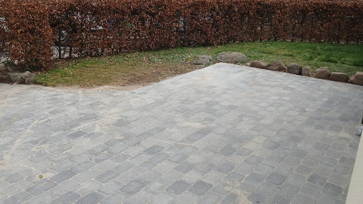 En grusbelagt terrasse med en hæk og græsplæne i baggrunden.
