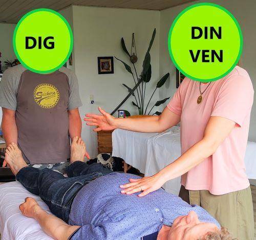 To personer udfører en behandling på en liggende mand i et lyst rum med planter og massageborde.