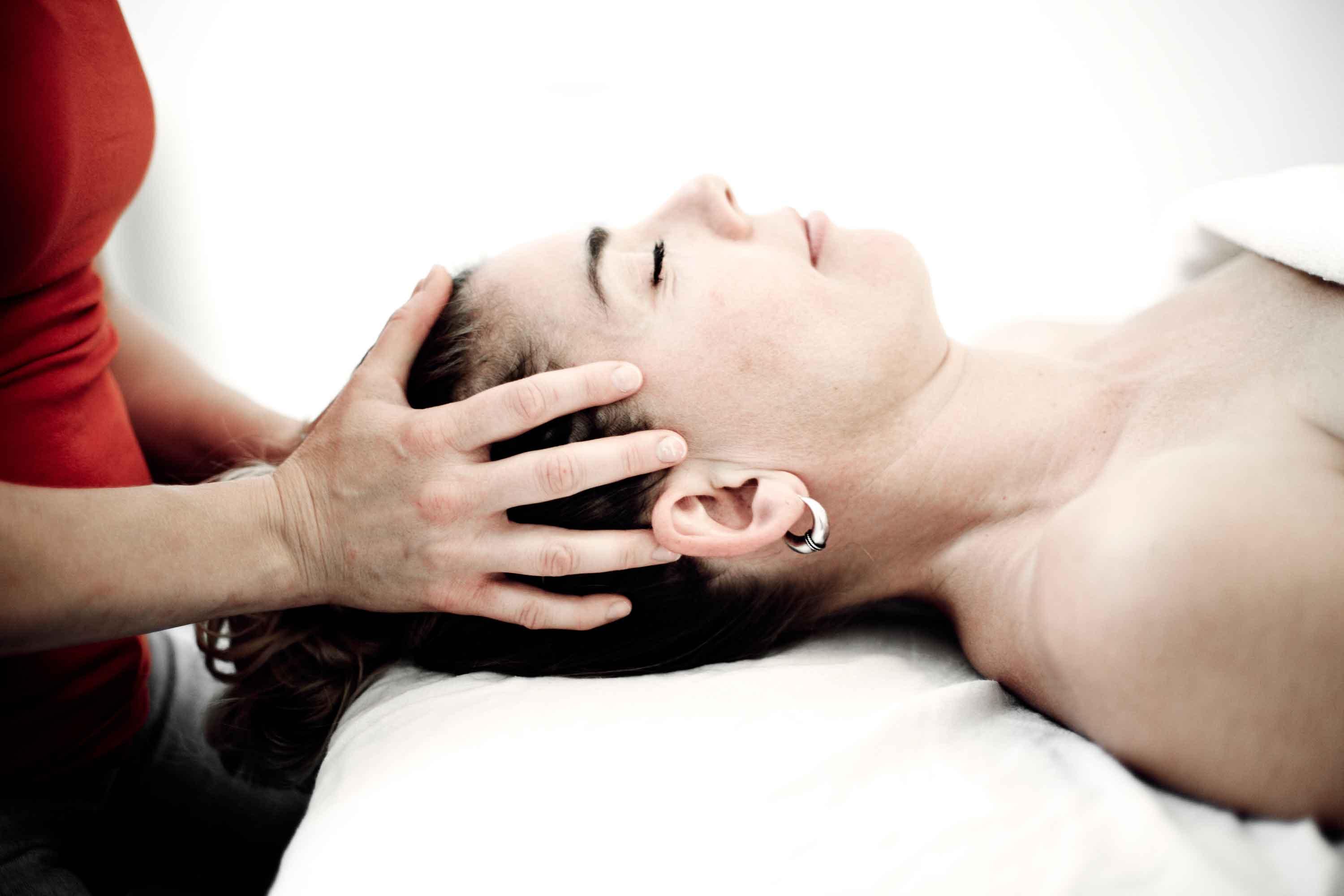 En kvinde får en afslappende hovedbundsmassage i en spa, mens hun ligger på en hvid pude.