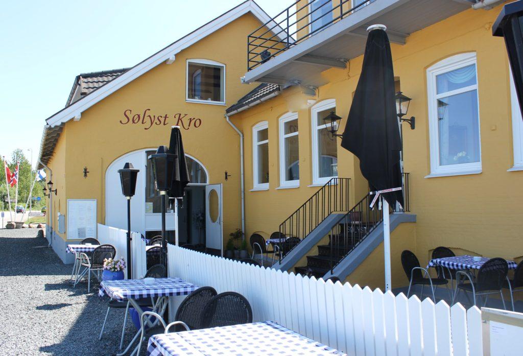 En solrig café med udendørs siddepladser, gule vægge og parasoller ved Sølyst Krog.