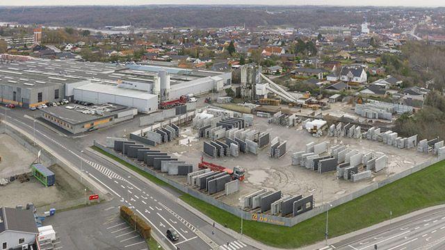 Luftfoto af en industriområde med lagerbygninger og betonblokke, omgivet af veje og boligområder.