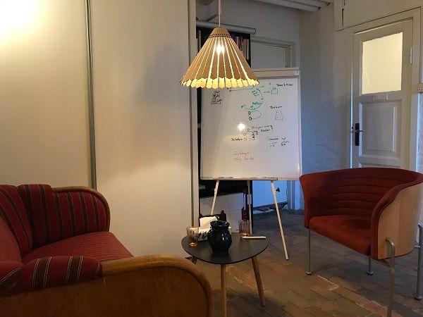 Et hyggeligt mødelokale med en sofa, to stole, et bord og en tavle med noter.