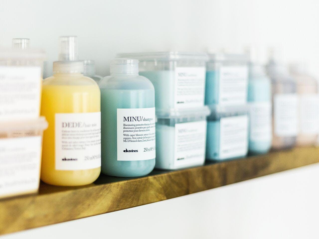 Flasker med farvet shampoo og balsam på en hylde i et moderne badeværelse.