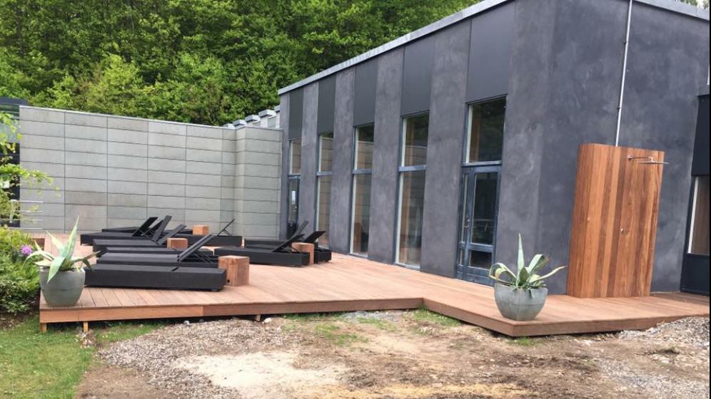 Moderne hus med terrasse, loungemøbler og planter i potter, omgivet af grønne træer.