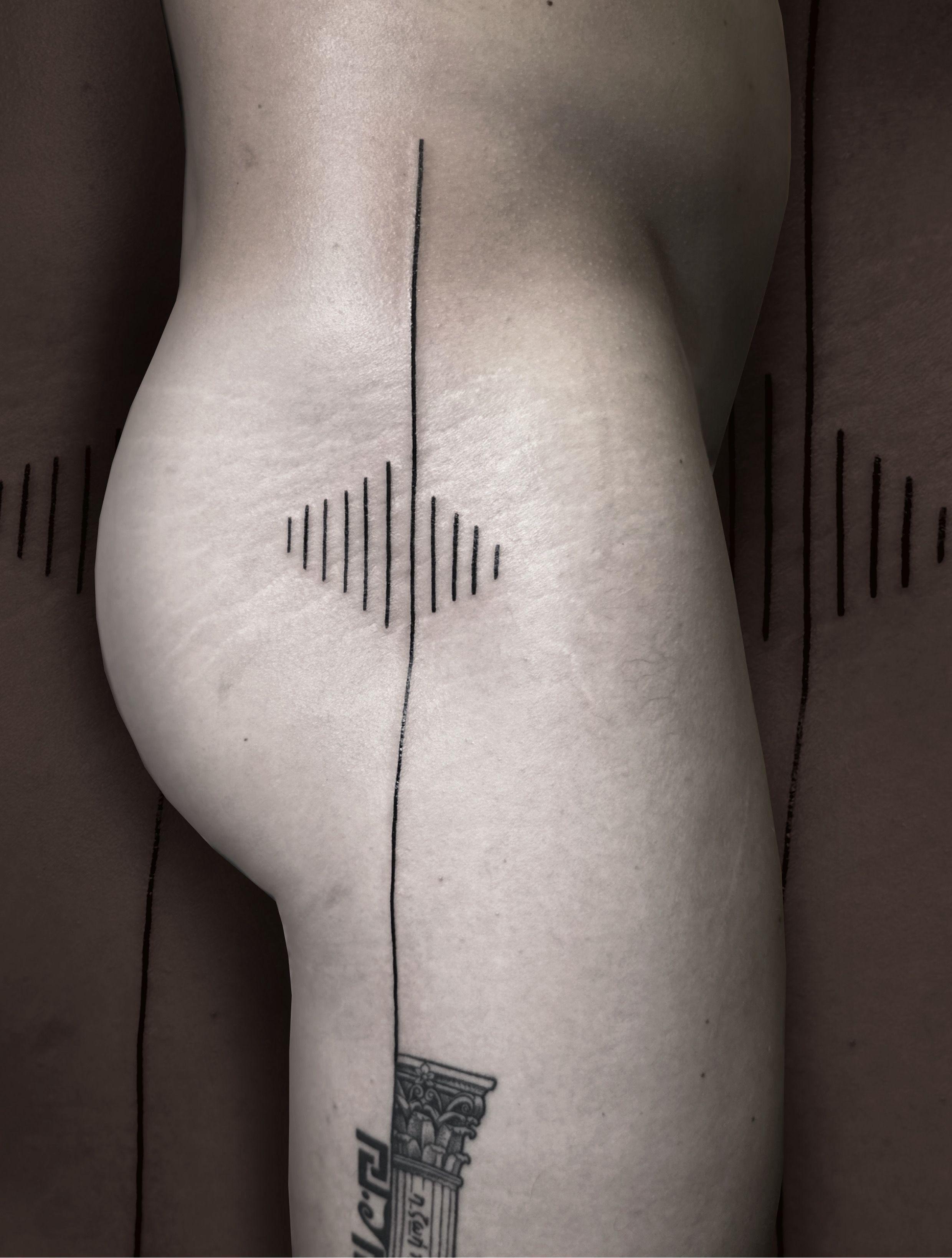 Tatovering på en persons lår med geometriske linjer og former, der skaber en visuel effekt.