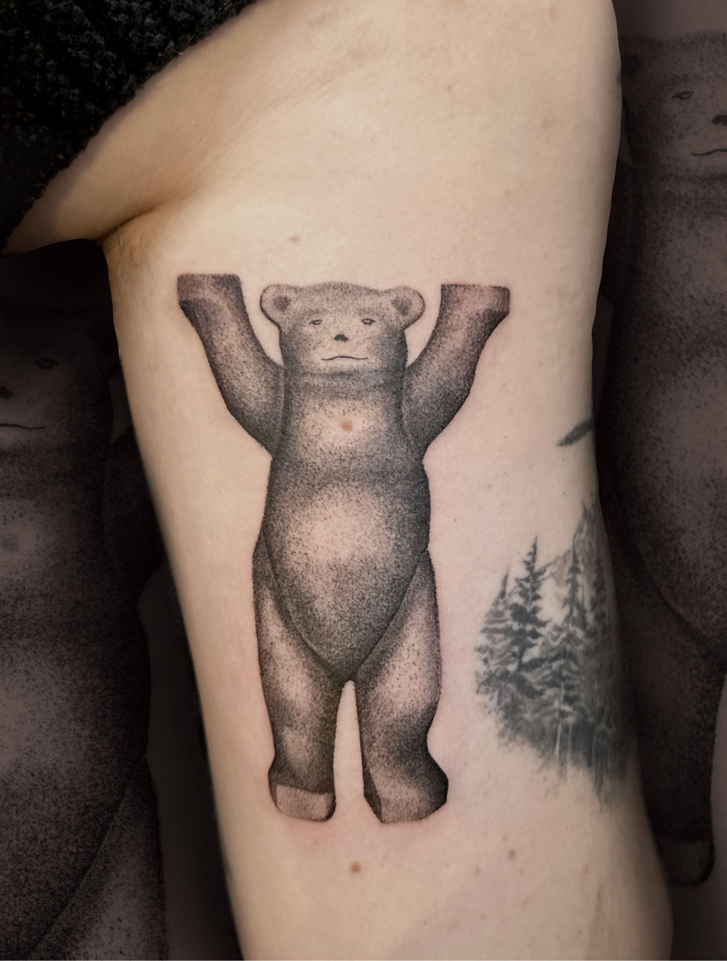 Tatovering af en bjørn med udstrakte arme på en arm, detaljeret med skygger og tekstur.