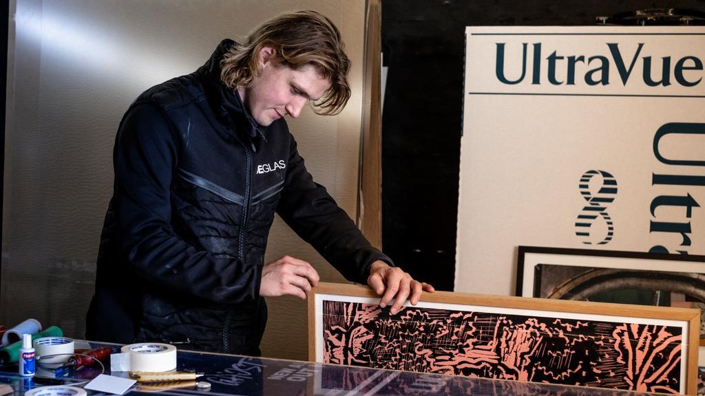 En mand arbejder med en ramme og kunstværk i et moderne atelier med UltraVue-logo i baggrunden.