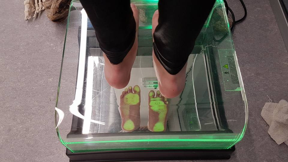 En person står barfodet på en glasplade, der viser fodaftryk med grønne lys.