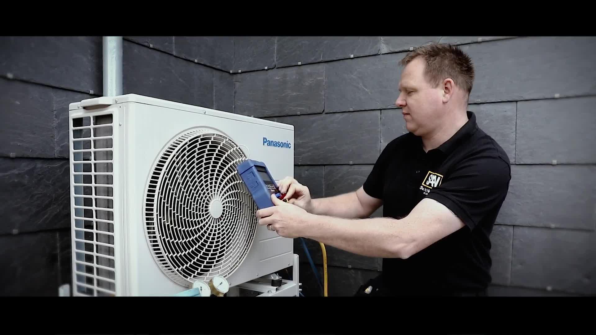 En tekniker måler temperaturer på en varmepumpe i et moderne rum med mørke vægge.