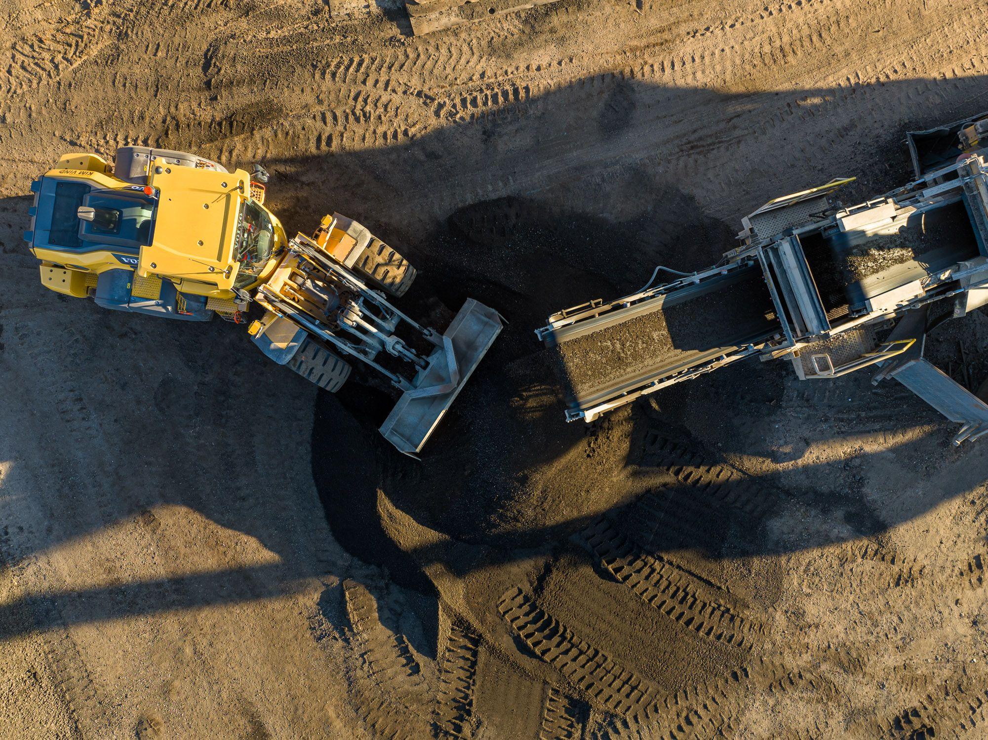 En gule bulldozer arbejder på en byggeplads og flytter sand til en transportbånd.