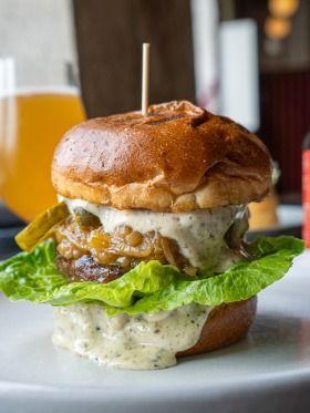 En saftig burger med salat, syltede agurker og en cremet dressing i en blød bolle.