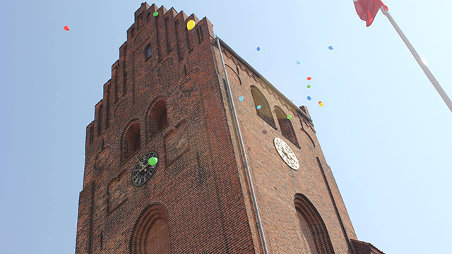 En høj murstensbygning med klokketårn og farverige balloner svævende i luften.