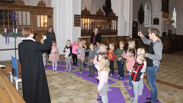 Børn synger og deltager i en aktivitet i en kirke, mens voksne ser til i baggrunden.