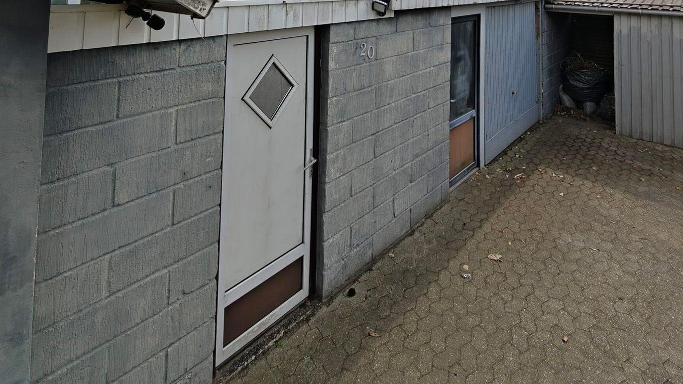 En grå murstensvæg med en hvid dør og vinduer, der fører til en garage eller kælder.