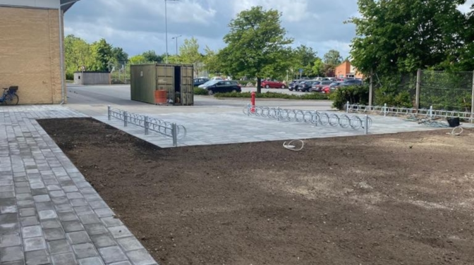 Cykelparkering med metalstativer og nyanlagt grusareal ved en bygning i et boligområde.