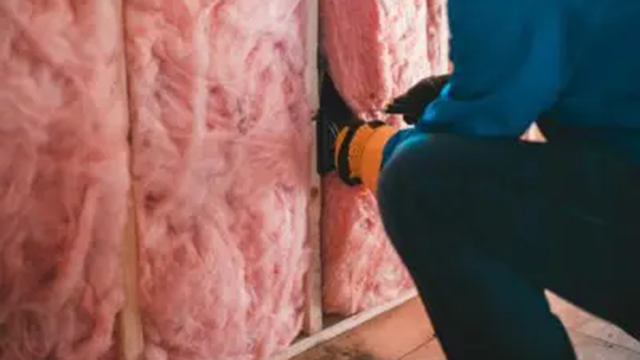 En håndværker installerer isolering i en væg med pink glasuld.