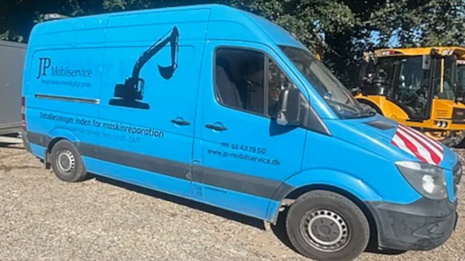 Blå varevogn med JP Mobilservice logo og kran, parkeret på en byggeplads.