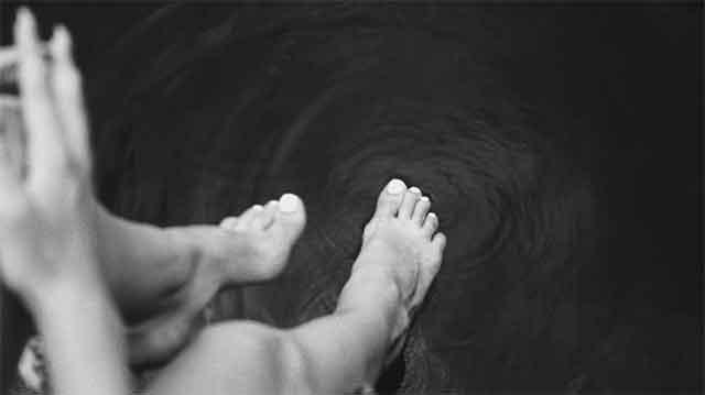 Toes dipping into dark water, creating gentle ripples around the feet in a serene setting.