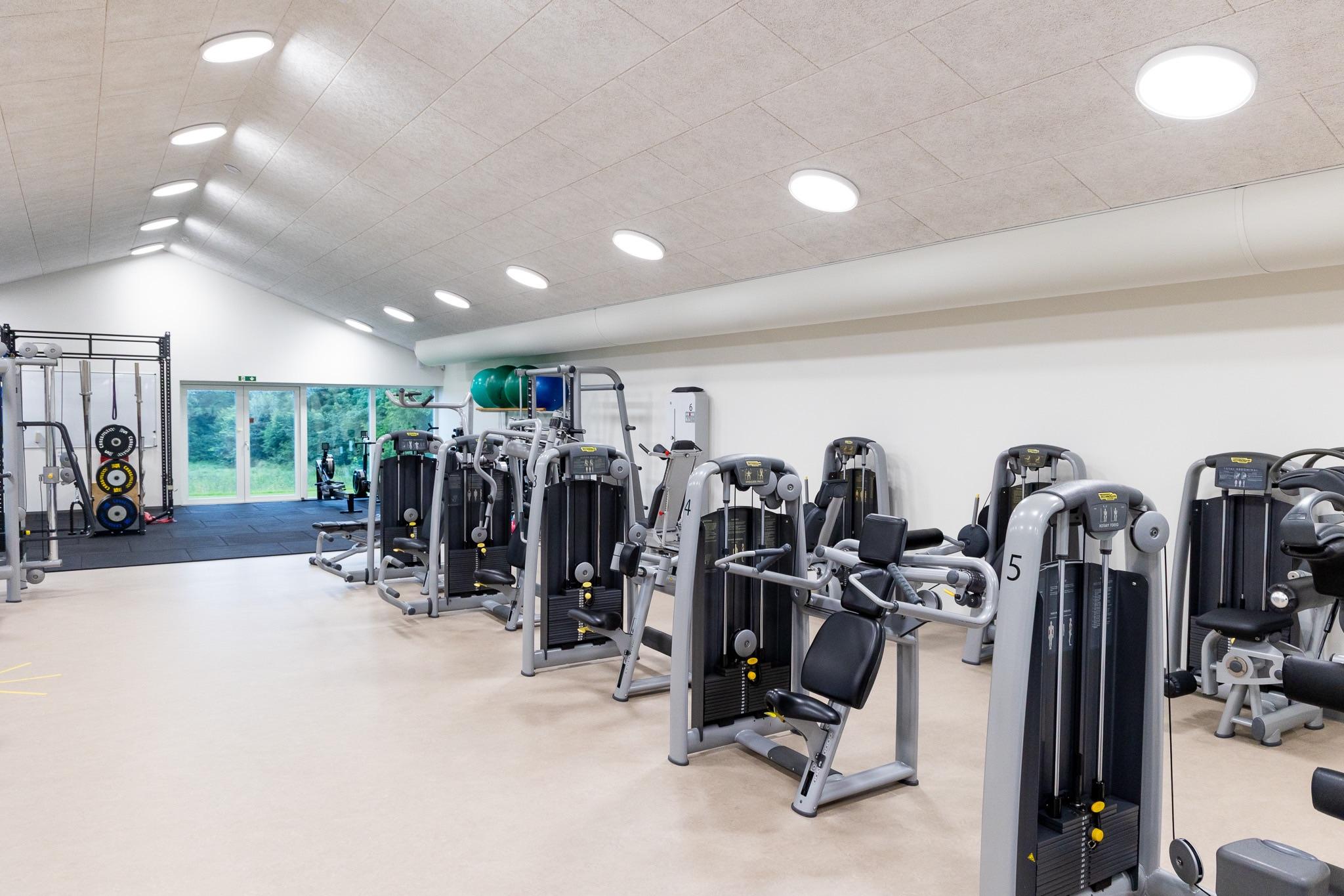 Moderne fitnesscenter med træningsmaskiner og vægte i et lyst rum med store vinduer.