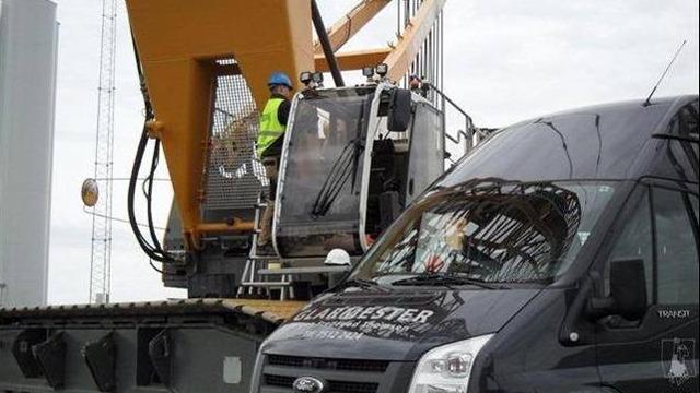 En kran arbejder på en byggeplads med en lastbil i forgrunden og en arbejder iført sikkerhedsudstyr.