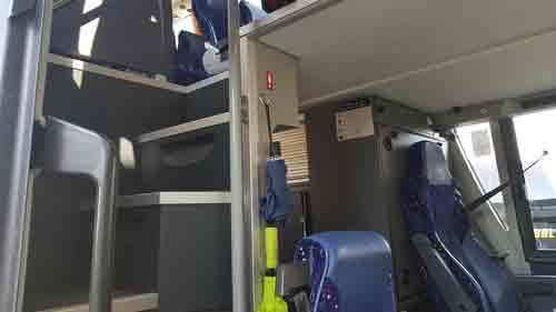 Indvendig udsigt af en bus med trapper og blå sæder, der viser passagerområdet og førersædet.